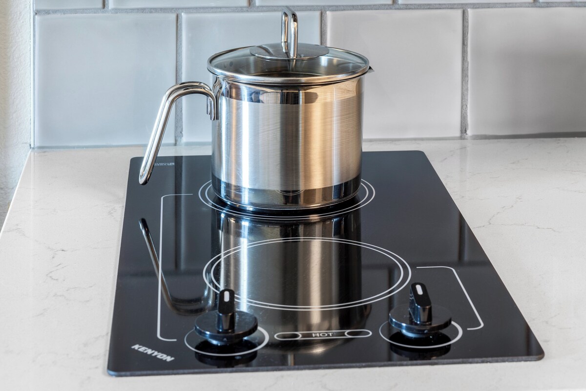 A stainless steel pot on a black induction cooktop with a handle and a lid.
