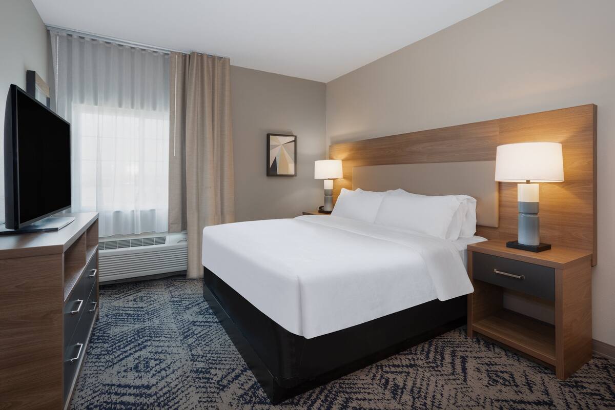 A hotel room with a bed, bedside tables, a TV, and a window with curtains.