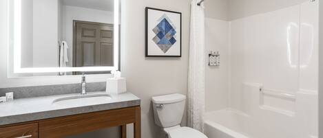 A modern bathroom with a large mirror, a sink, a toilet, and a bathtub.