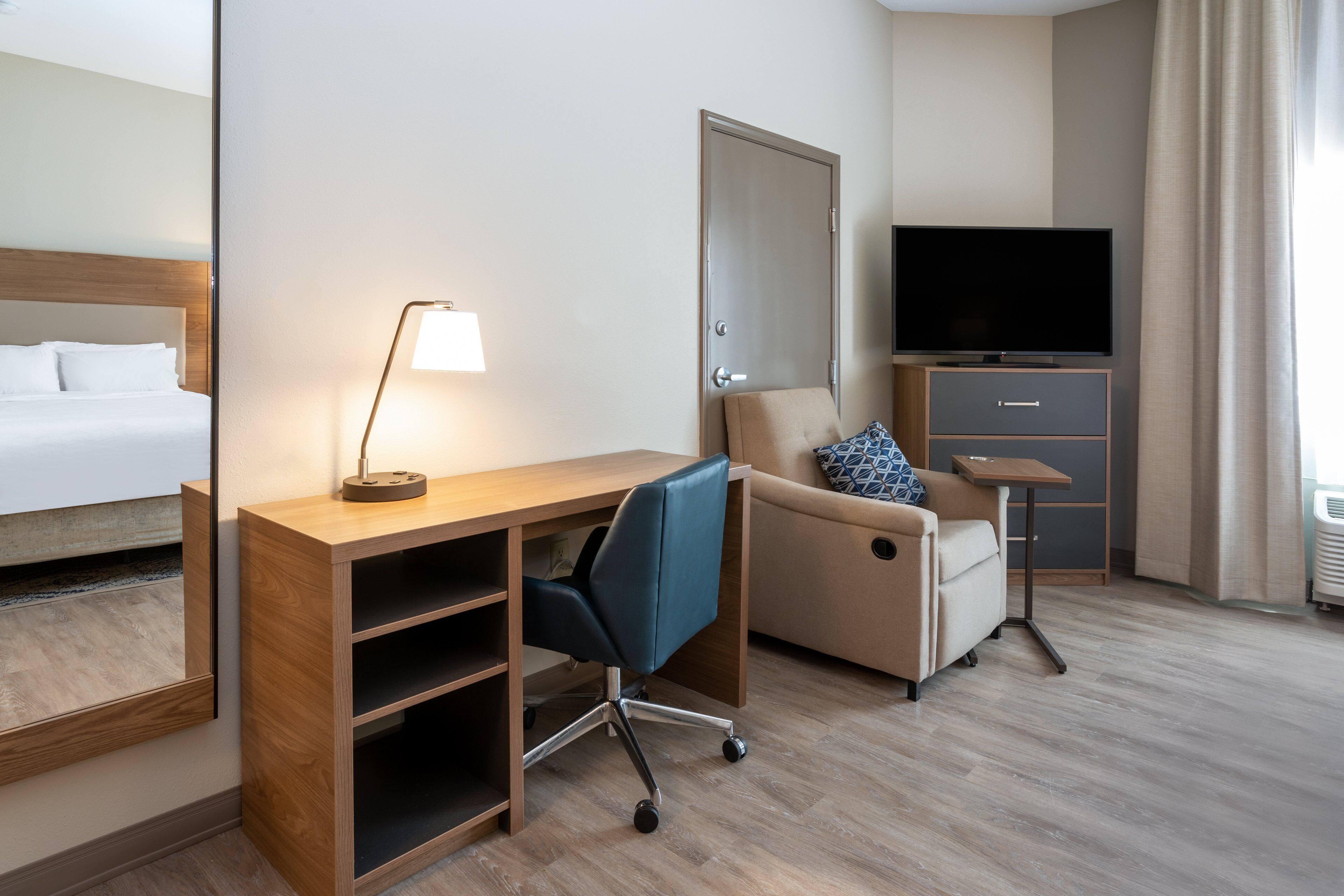 Habitación de hotel con cama, escritorio, silla, televisor y una pequeña mesa.