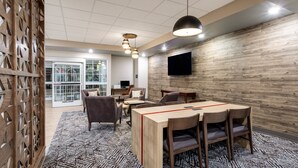 A modern meeting room with a wooden table, chairs, a patterned carpet, and a mounted TV on the wall. - Candlewood Suites Grand Junction by IHG (Grand Junction)