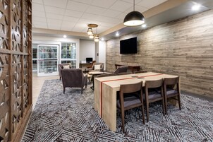 Una sala de reuniones moderna con una mesa de madera, sillas, una alfombra estampada y un televisor montado en la pared.