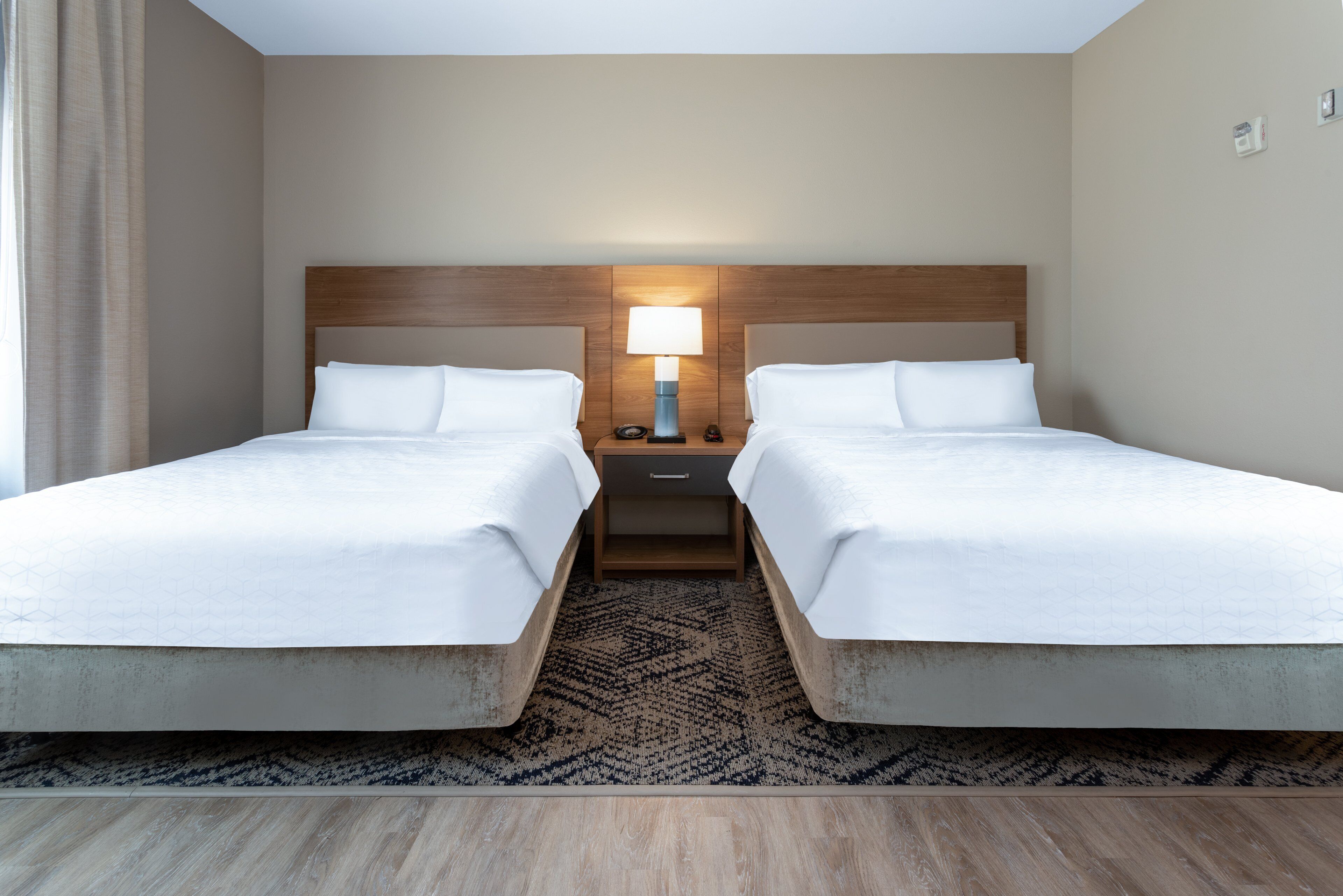 A hotel room with two beds, a nightstand with a lamp, and a patterned rug.
