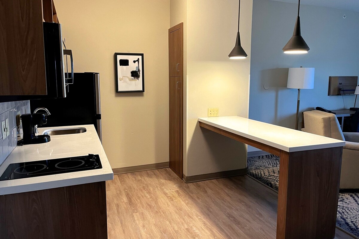 A modern kitchen with a built-in stove, wooden cabinets, a white countertop, and pendant lighting.
