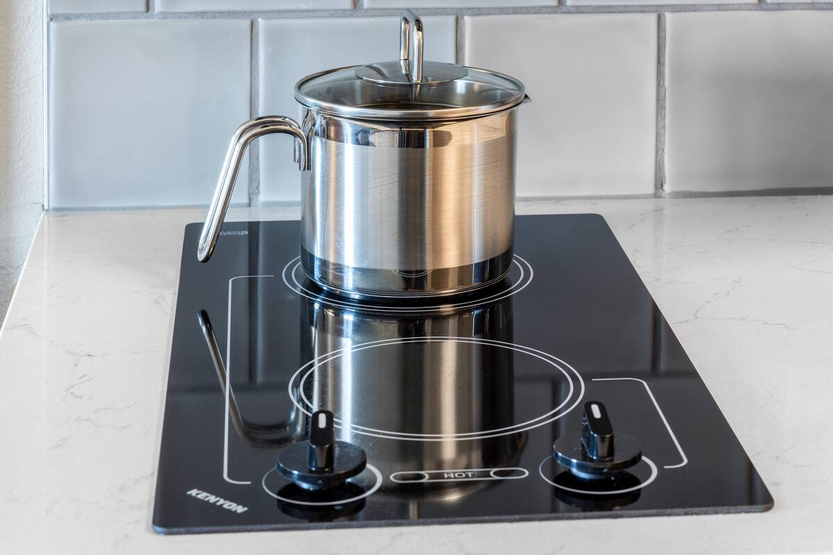 A stainless steel pot on a black induction cooktop with a handle and a lid.