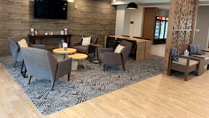 A modern hotel lobby with a wooden wall, a flat-screen TV, a bar area, and a seating arrangement with tables and chairs. - Candlewood Suites Grand Junction by IHG (Grand Junction)