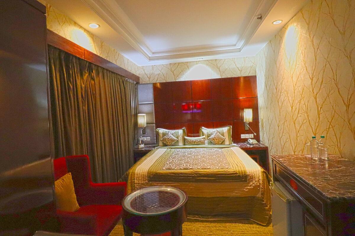 Una habitación de hotel con una cama grande, un sillón rojo, una mesita redonda y una mesita auxiliar de mármol.
