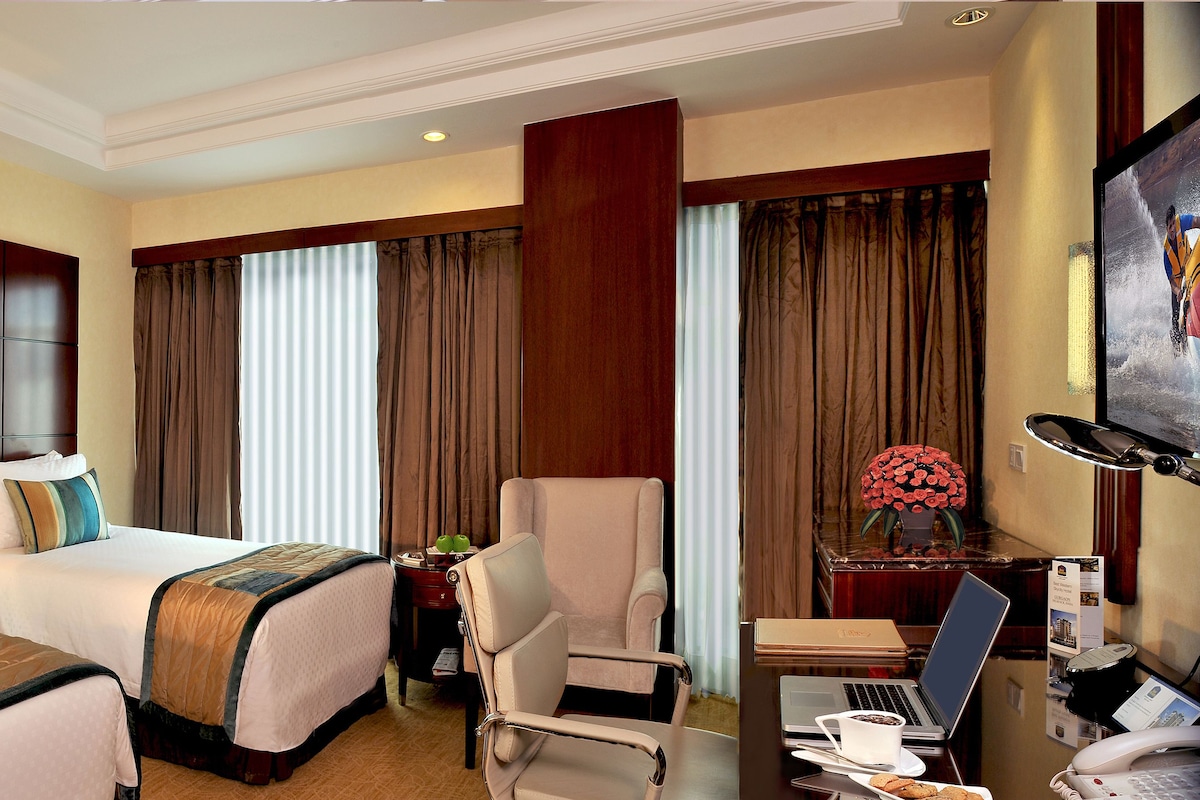 A hotel room with two beds, a desk with a laptop, a chair, and a TV.