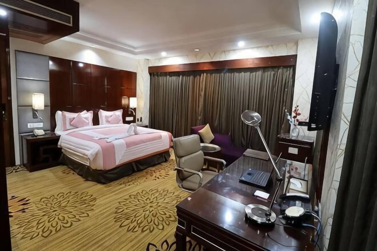Una habitación de hotel con cama, escritorio con lámpara, silla, mesita de noche y televisor.