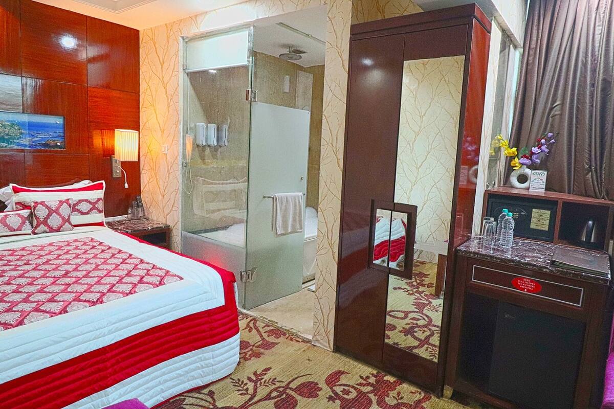 Habitación de hotel con cama, escritorio, espejo y zona de ducha.