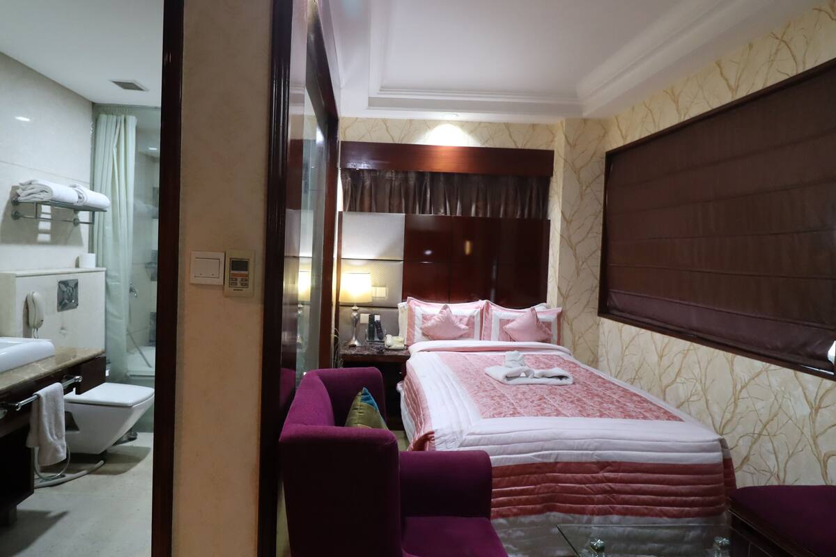 Habitación de hotel con cama, una silla, tocador con espejo, inodoro y zona de ducha.