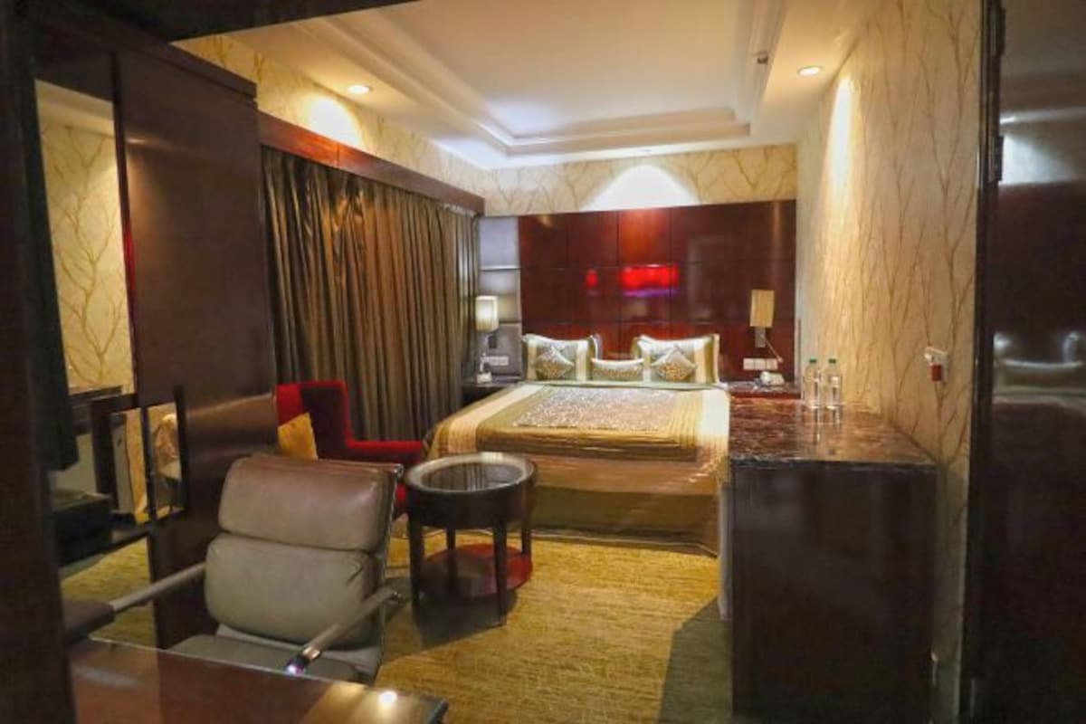 A hotel room with a bed, a desk, a chair, a small table, and a TV.