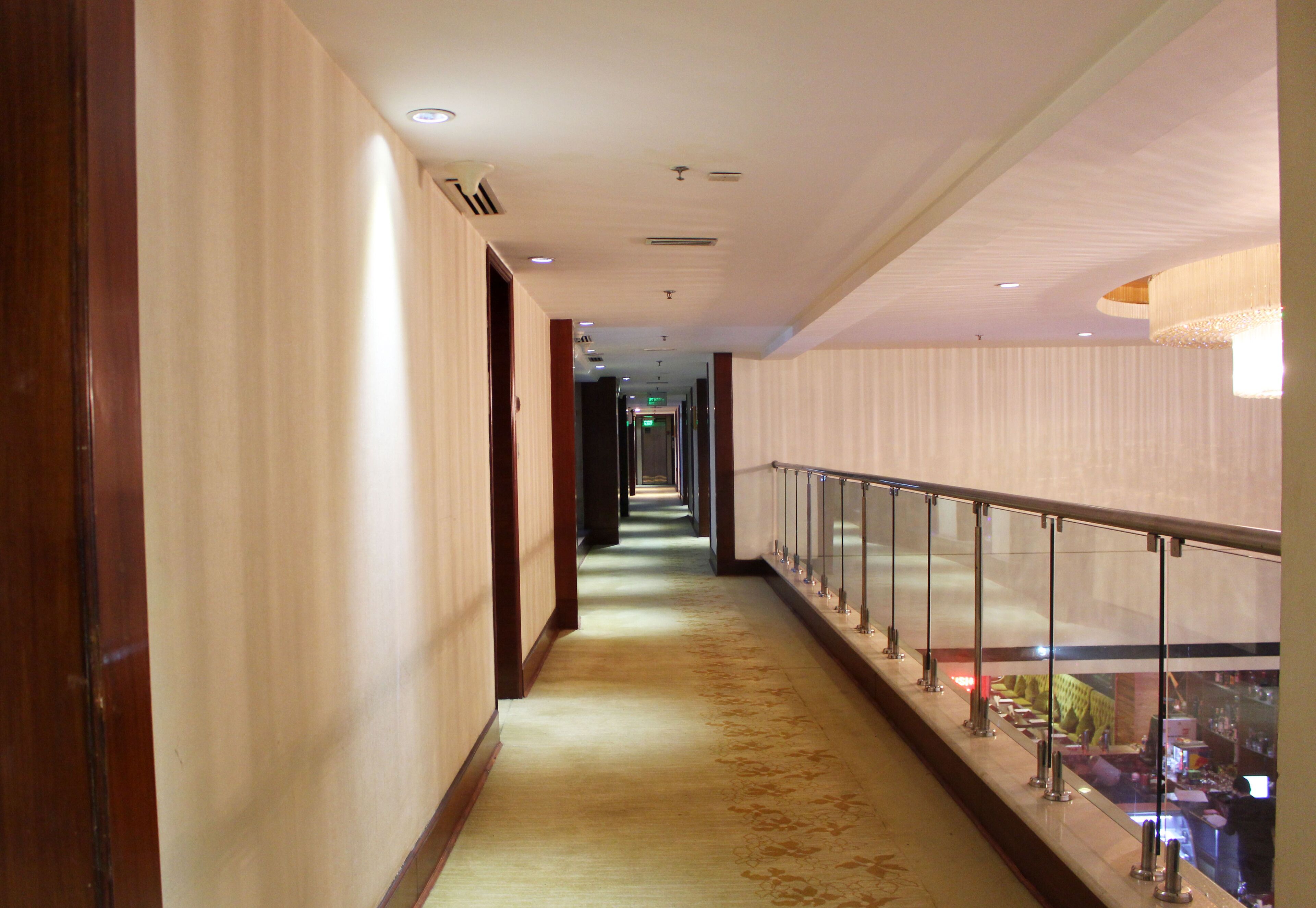 Un couloir d'hôtel avec un sol recouvert de moquette, des portes en bois et une rambarde en verre sur le côté droit.