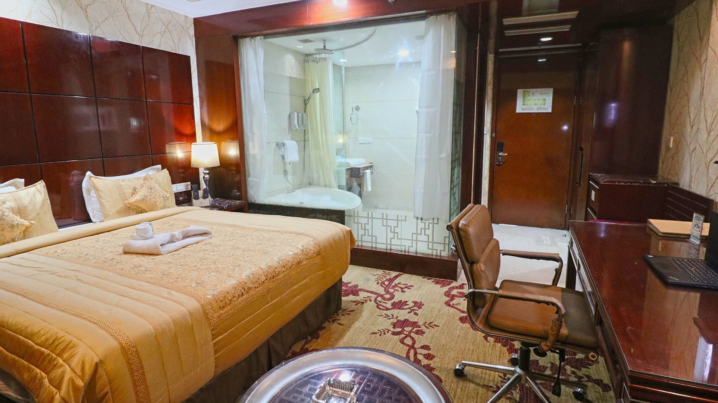 A hotel room with a large bed, a desk with a laptop, a chair, a shower area, and a bathroom.