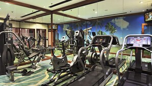 A gym with various exercise machines, a mirrored wall, and a tropical mural. - Skycity Hotel (Gurugram)