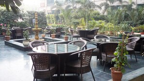 An outdoor seating area with wicker chairs and tables, surrounded by potted plants and a fountain. - Skycity Hotel (Gurugram)