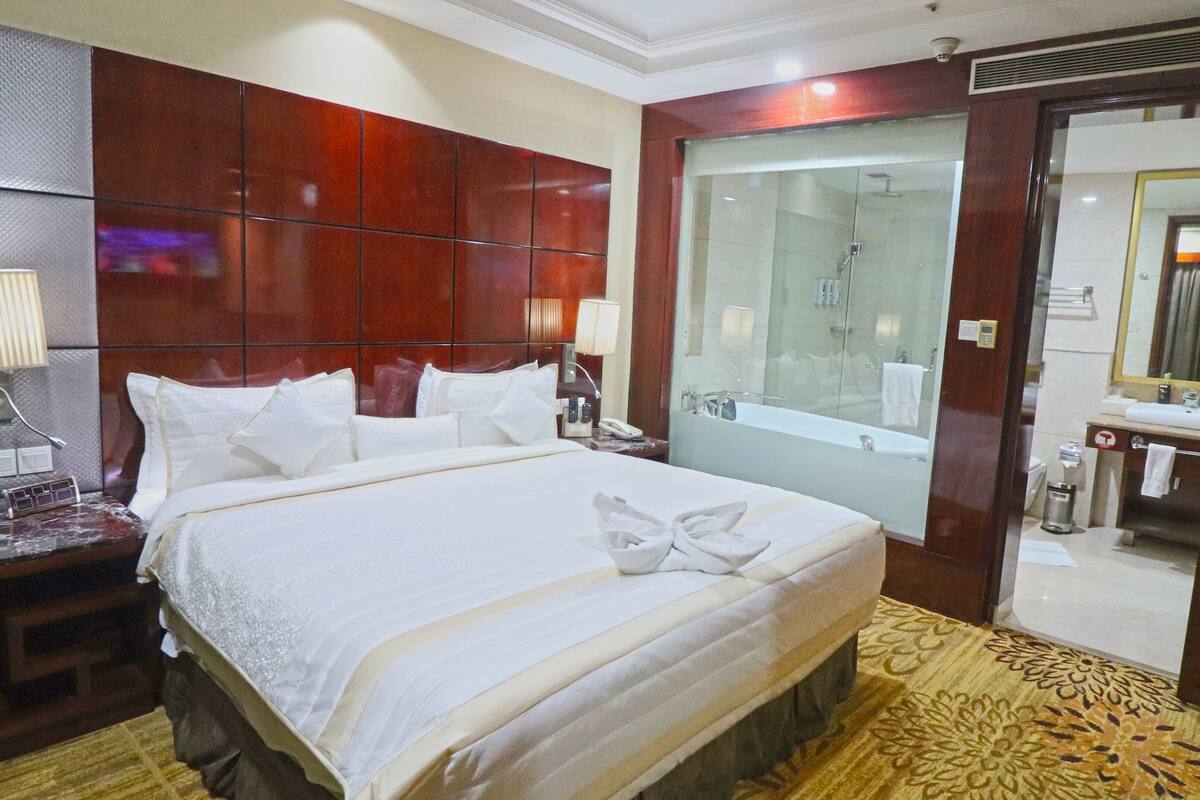Una habitación de hotel con una cama grande, una ducha con cerramiento de vidrio y un cabecero de madera.