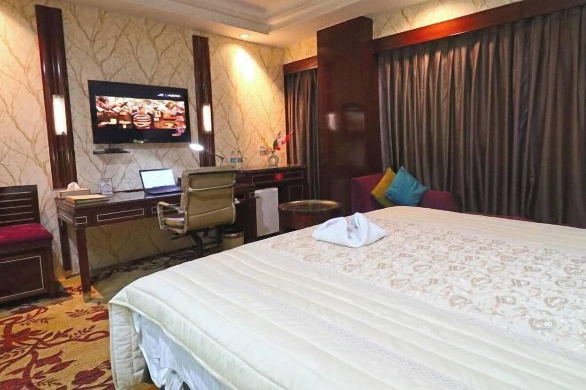 Una habitación de hotel con cama, escritorio, computadora, televisor y ventana con cortinas.