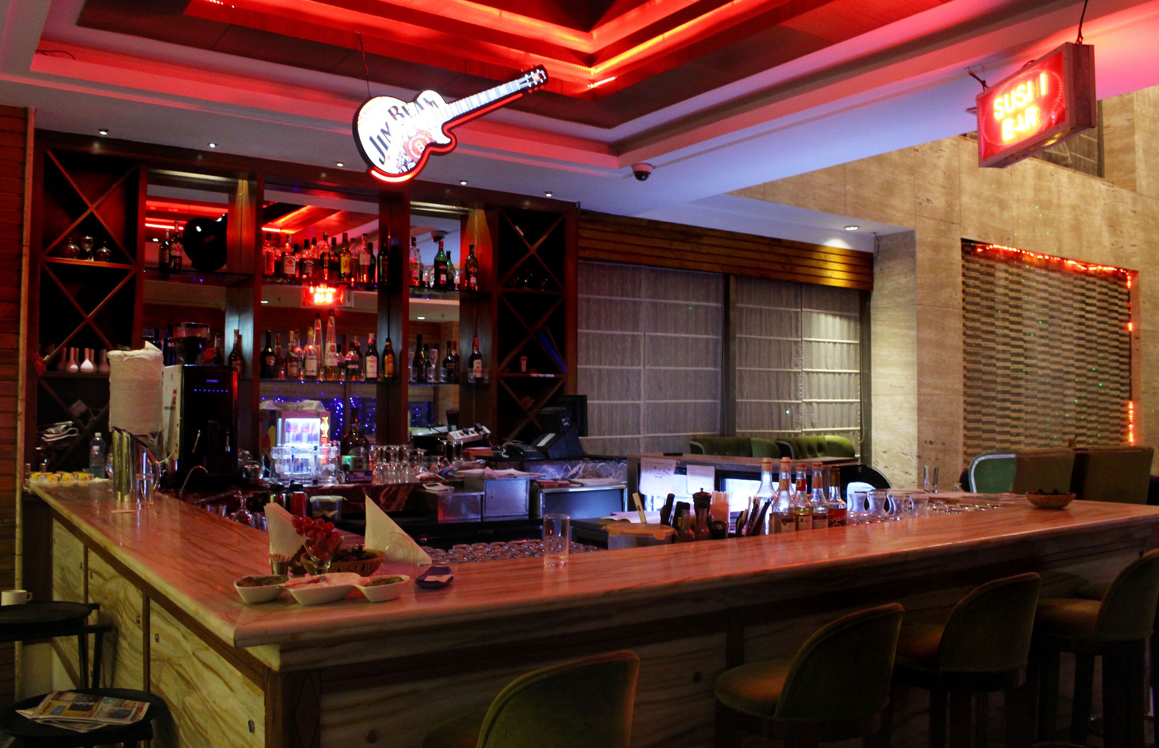 A bar area with a neon guitar sign, shelves with bottles, and a sushi bar sign.