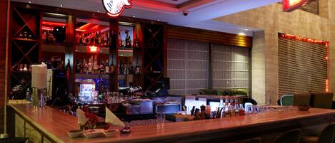 A bar area with a neon guitar sign, shelves with bottles, and a sushi bar sign.