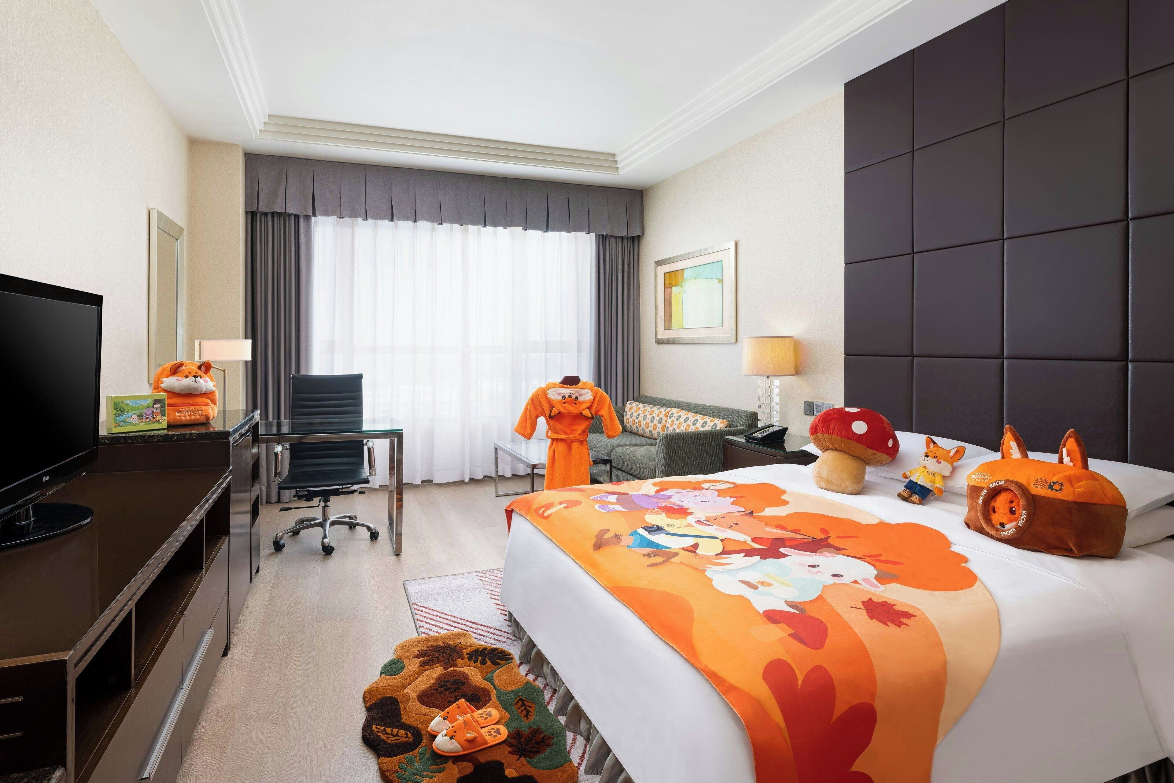 A hotel room with a large bed, a desk with a flat-screen TV, a chair, a sofa, and a window with curtains.