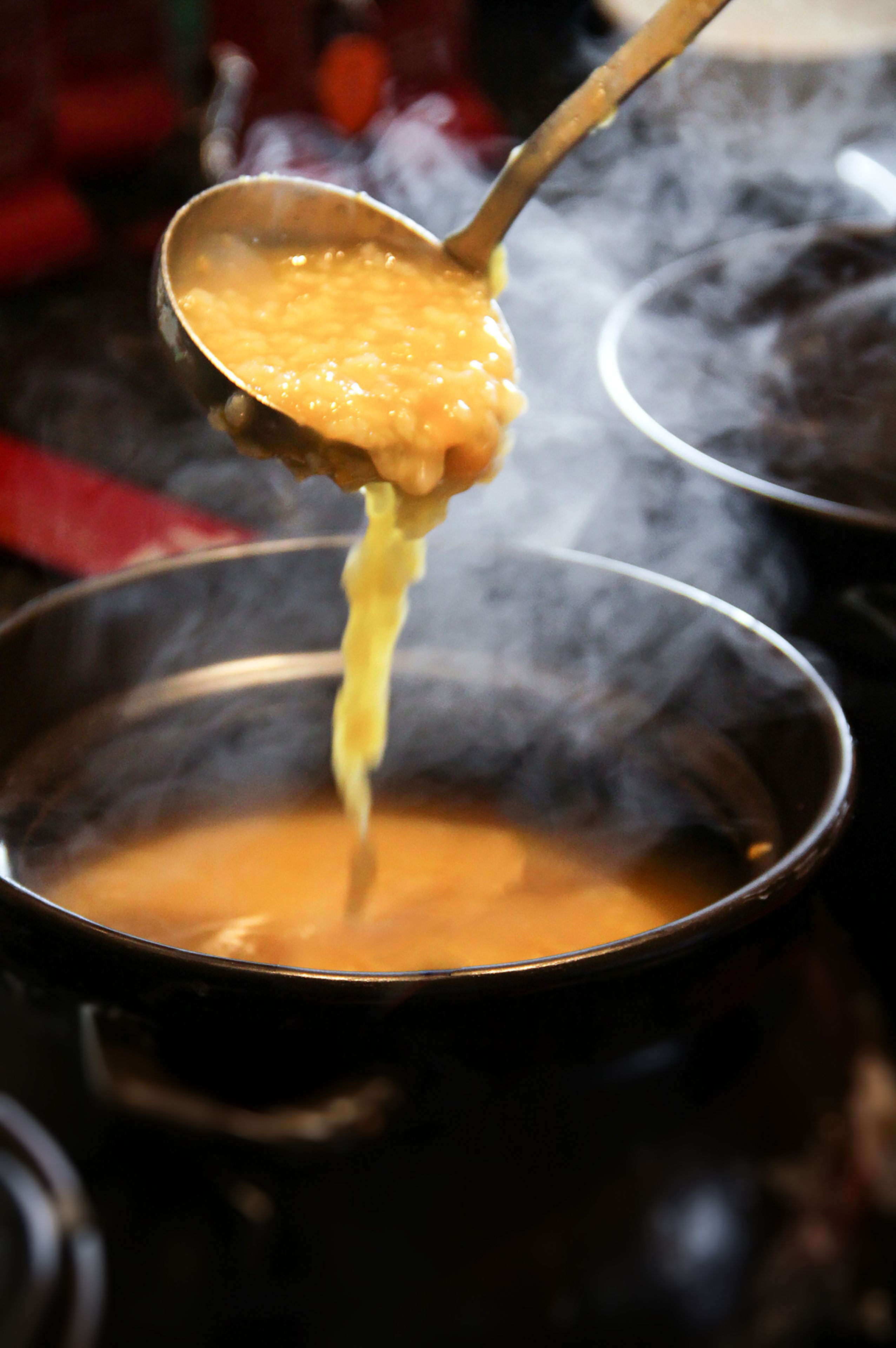 A ladle lifting a thick, orange-colored soup from a pot.
