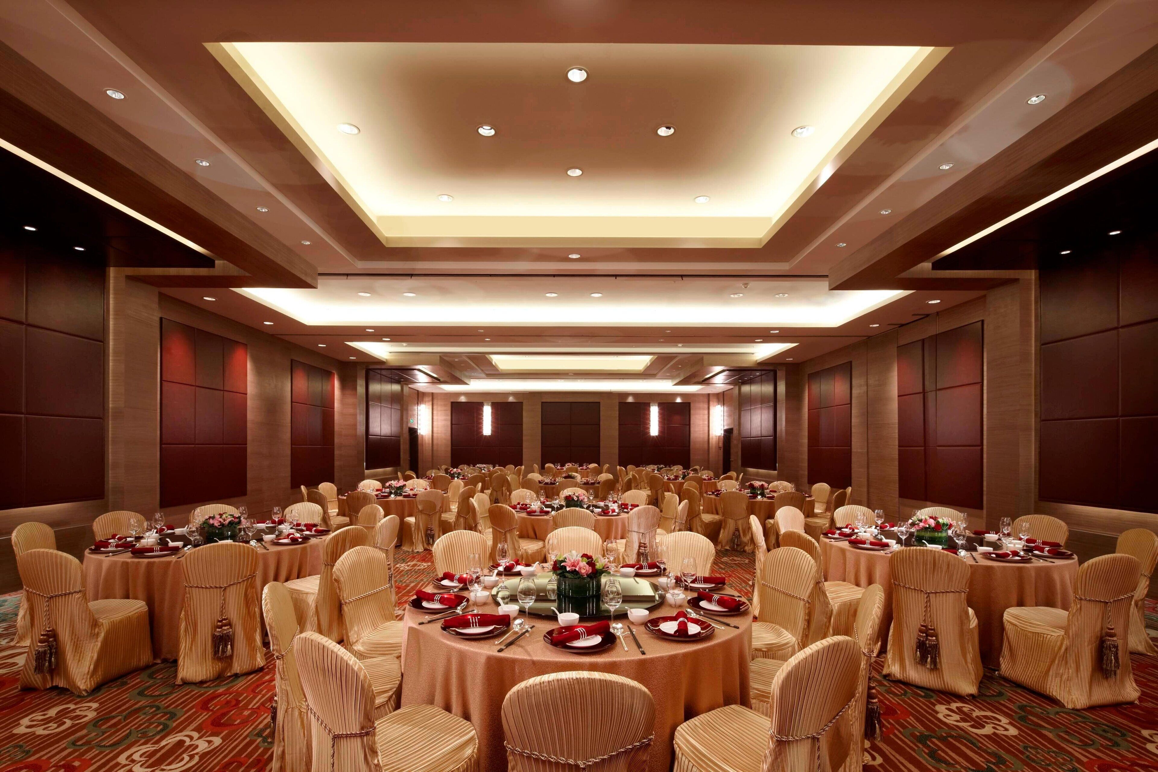 A banquet hall with round tables set for a formal event, surrounded by rows of chairs.