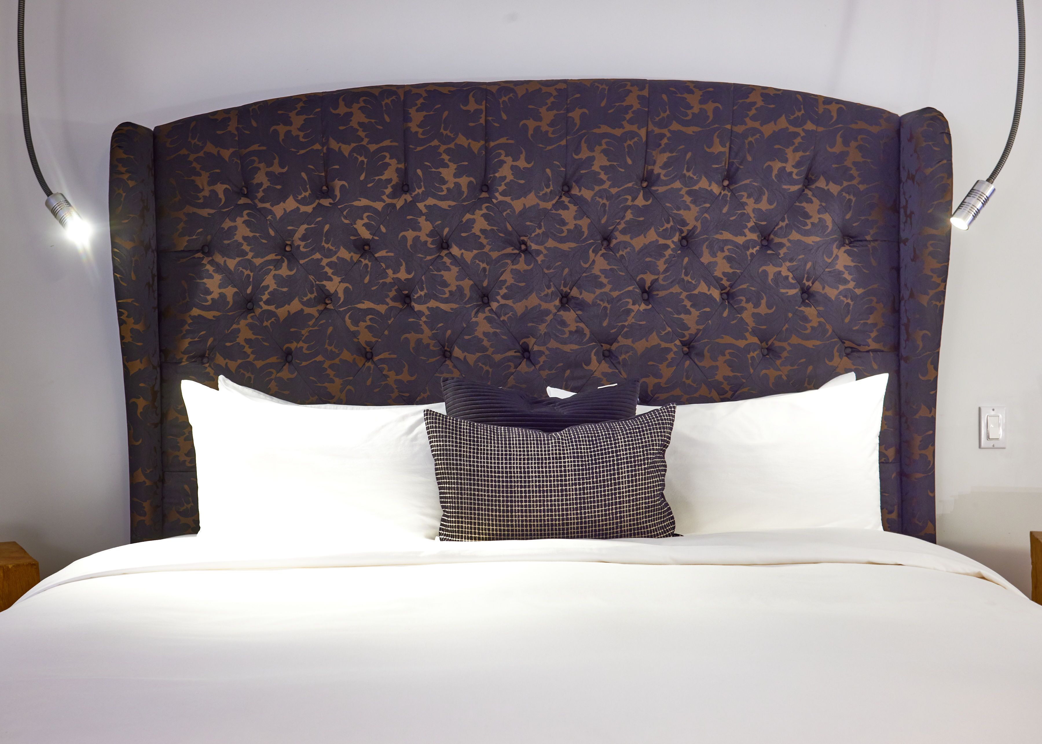A bed with a tufted headboard, white bedding, and a patterned pillow.