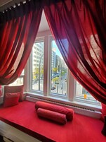Une chambre avec un lit rouge, une fenêtre avec des rideaux rouges et une vue sur une rue de la ville.