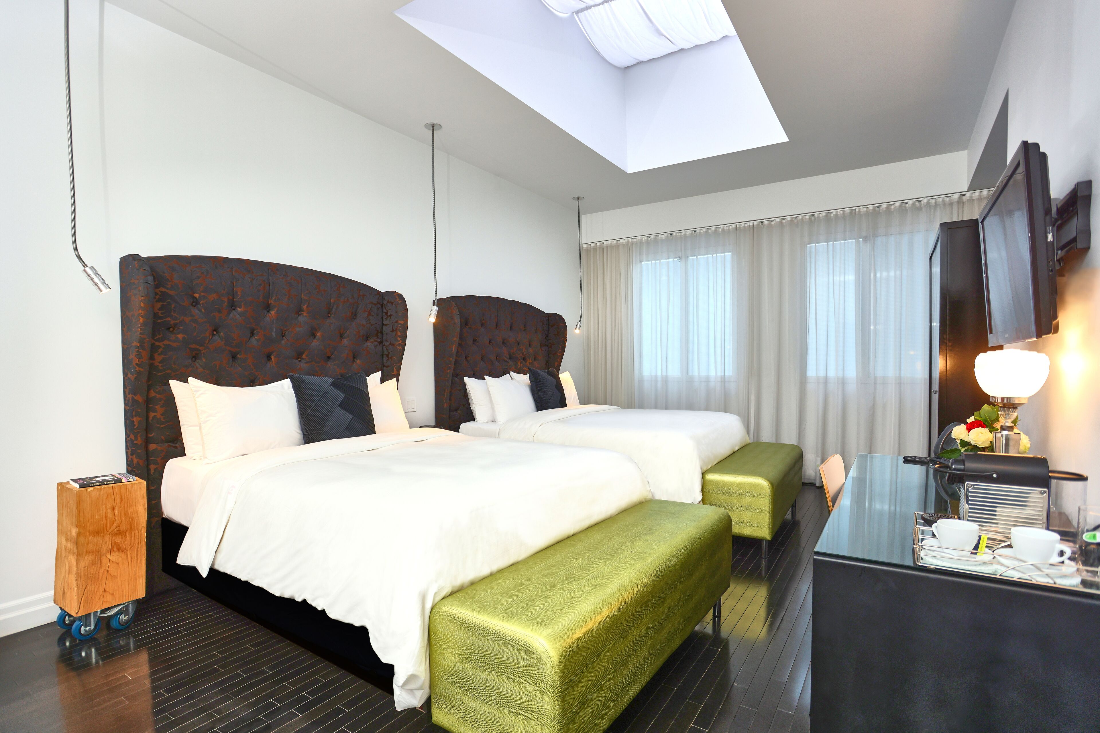 A hotel room with two beds, a desk, a chair, a TV, and a skylight.