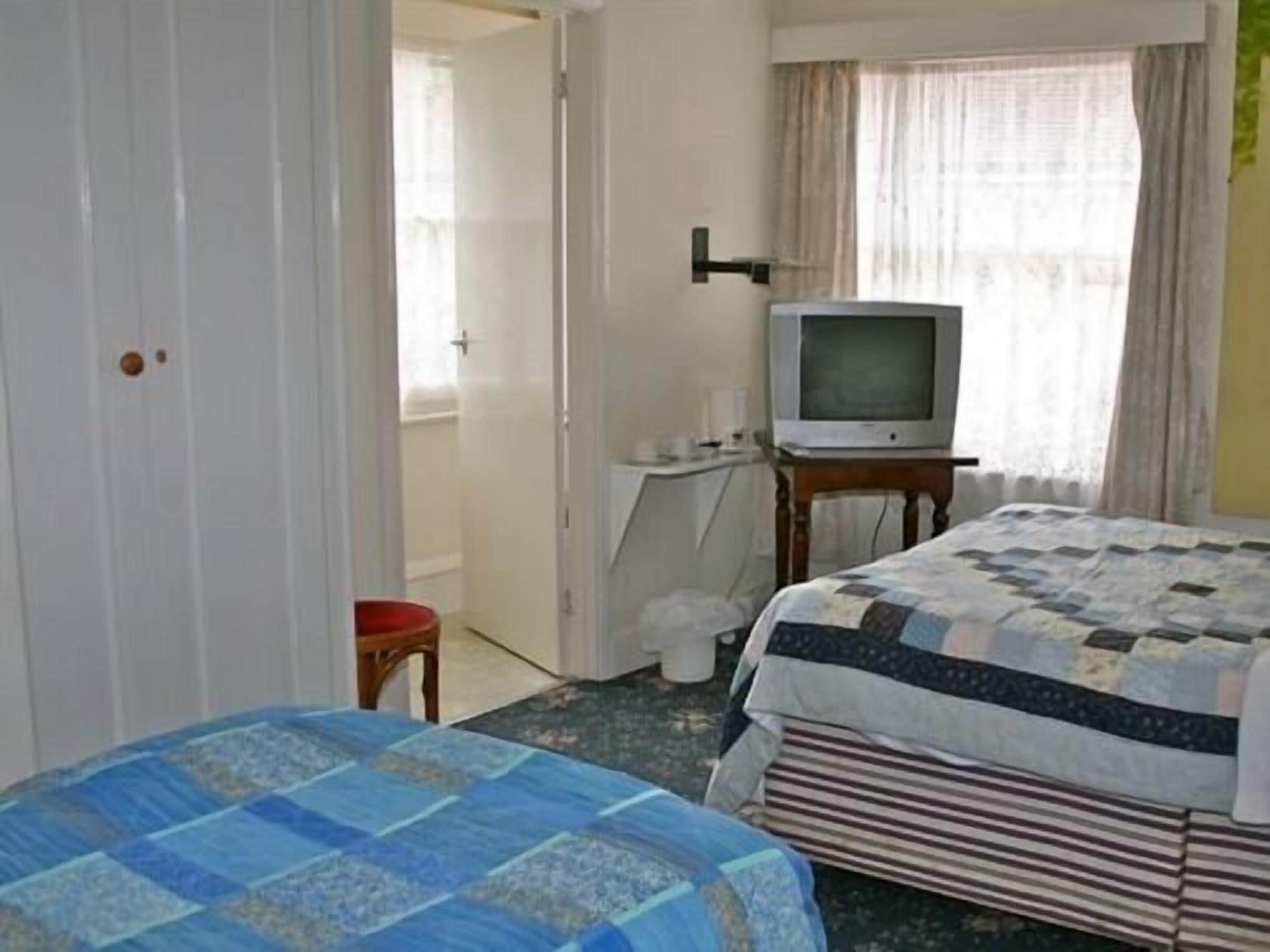A hotel room with a bed, a television, a small table, and a door leading to another room.