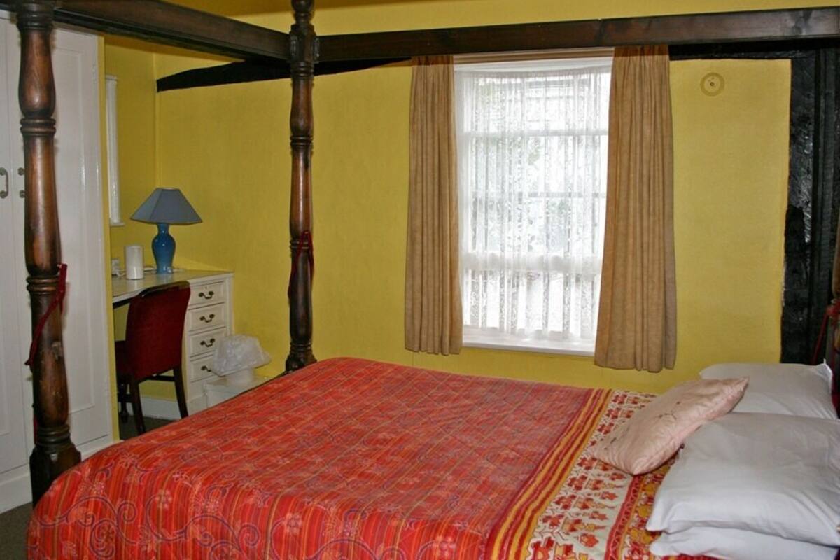 Une chambre à coucher avec un lit à baldaquin, un bureau avec une lampe et une fenêtre avec des rideaux.