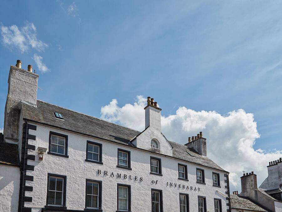 Un edificio blanco con el nombre "BRAMBLES OF INVERARY" en su fachada, que cuenta con varias chimeneas y ventanas.