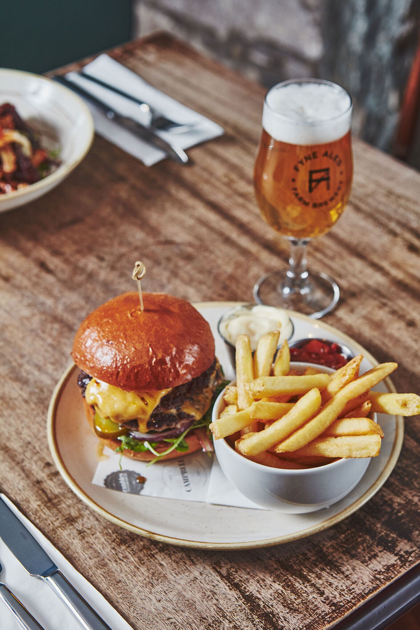 Hamburguesa con papas fritas y una cerveza en una mesa de madera.