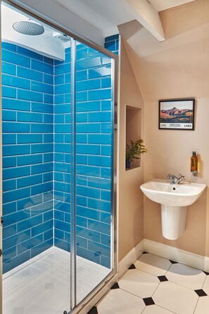 A bathroom with a blue-tiled shower enclosure, a white sink, and a framed picture on the wall.