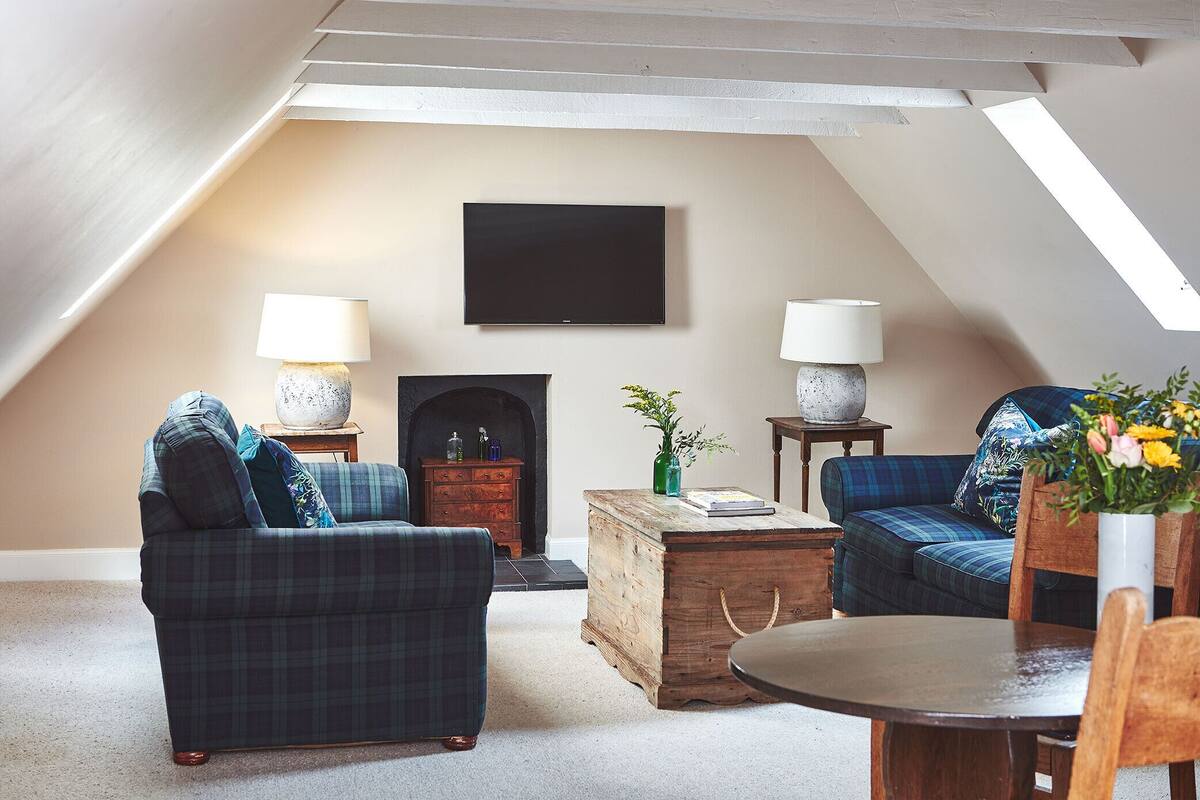 Un dormitorio tipo loft acogedor, con techo inclinado, chimenea, televisor de pantalla plana y comedor con mesa y sillas de madera.