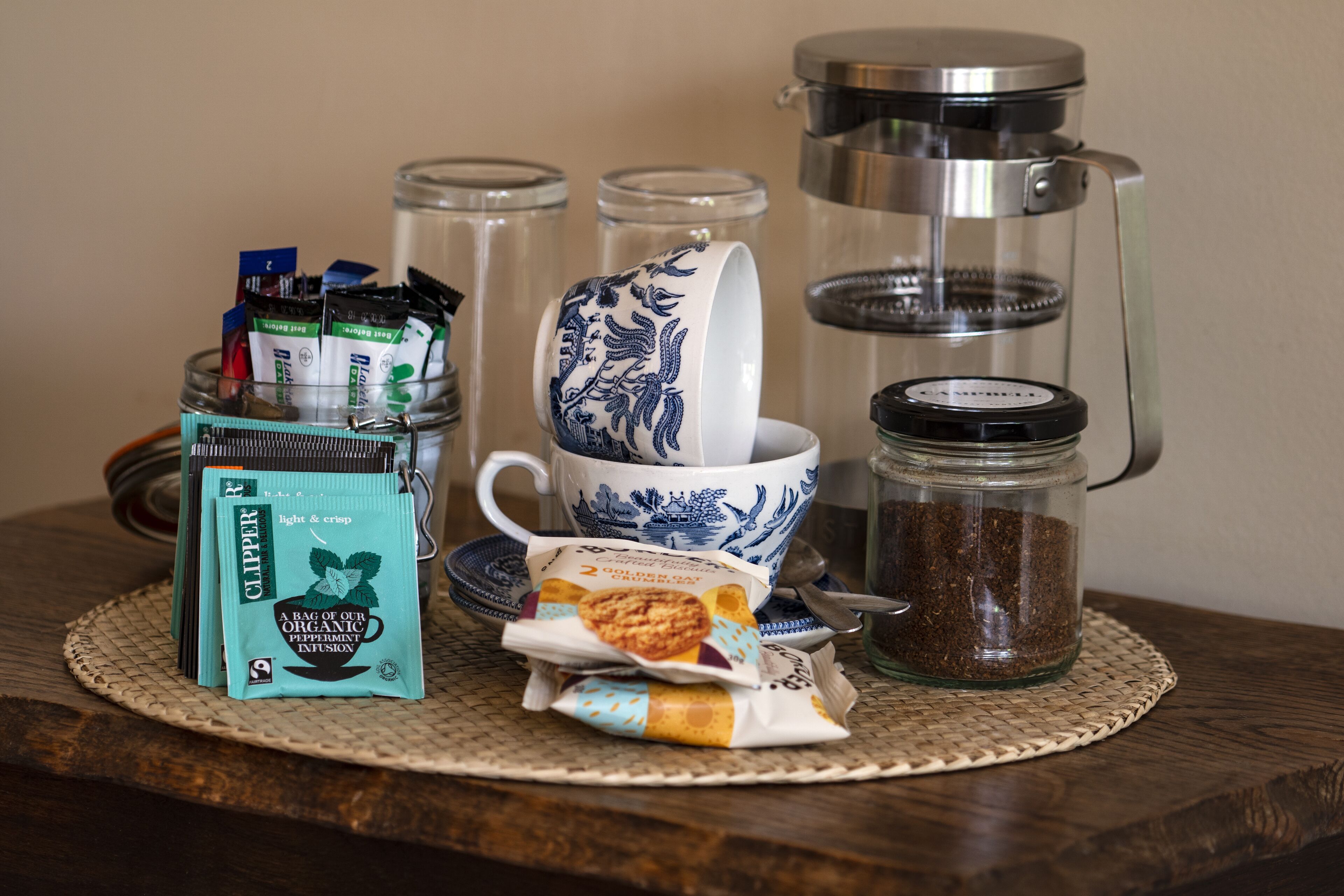 A table with a coffee maker, a cup, a jar of coffee, packets of tea, and a packet of organic peppermint infusion.