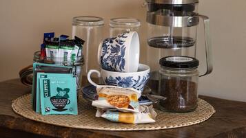 A table with a coffee maker, a cup, a jar of coffee, packets of tea, and a packet of organic peppermint infusion.
