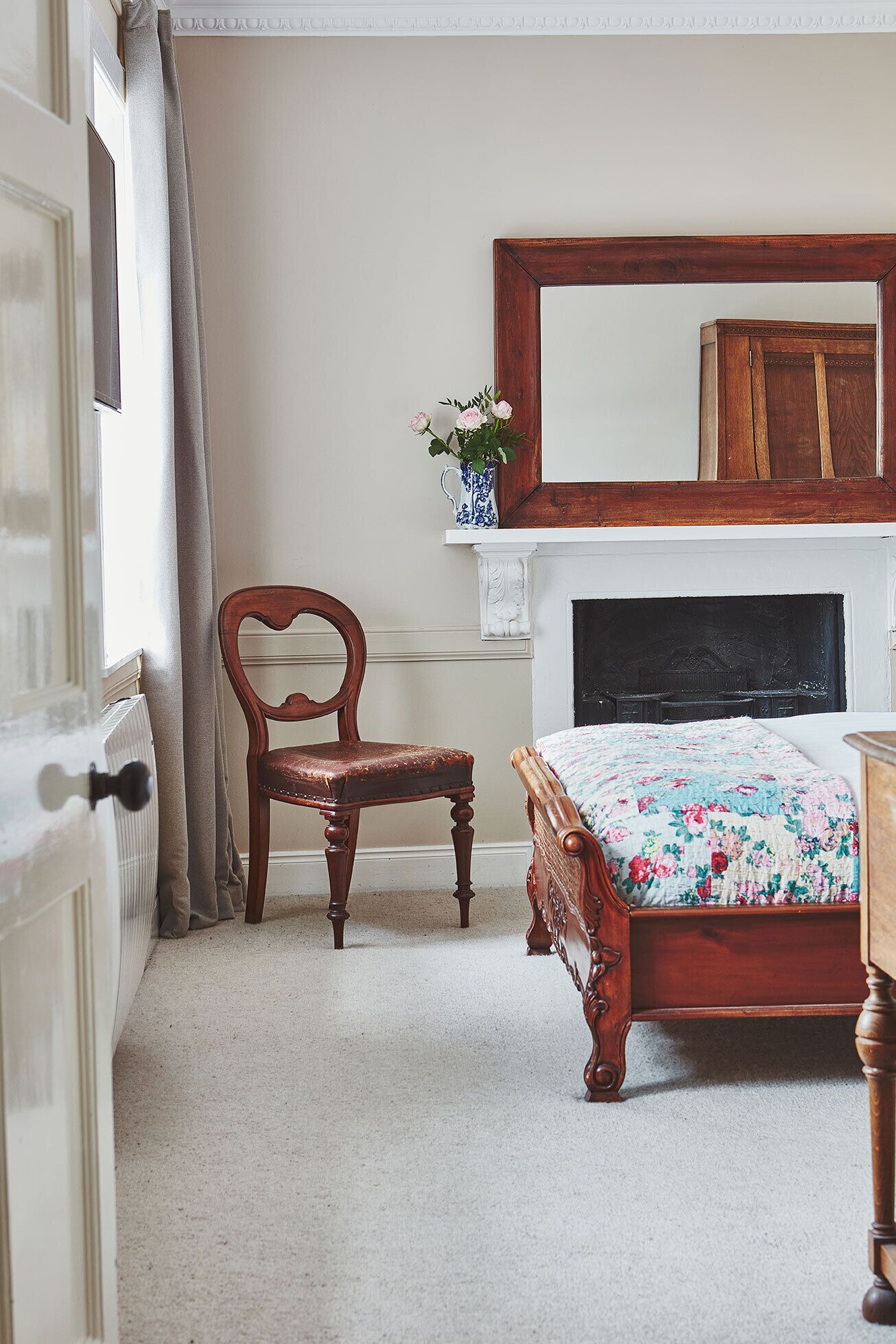A bedroom with a wooden bed, a chair, a dresser, and a mirror above the bed.