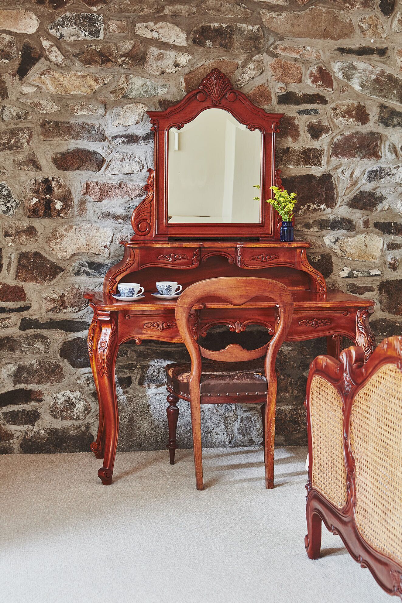 A wooden desk with a mirror, a chair, and a vase with flowers.