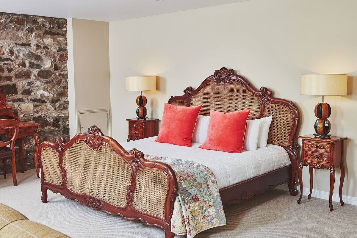 Un dormitorio con una cama de madera, dos mesitas de noche, una pared de piedra y una silla de madera.