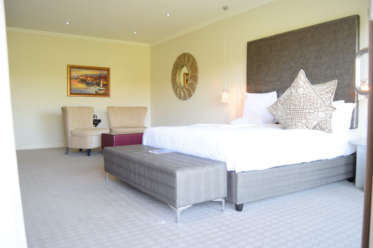 Een hotelkamer met een groot bed, een bankje, twee stoelen, een schilderij en een decoratieve spiegel.