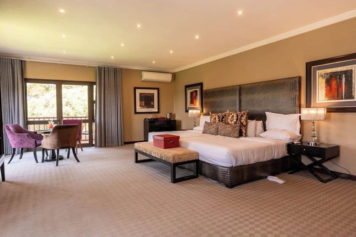Een ruime slaapkamer met een groot bed, een klein tafeltje, twee stoelen en een raam met gordijnen.