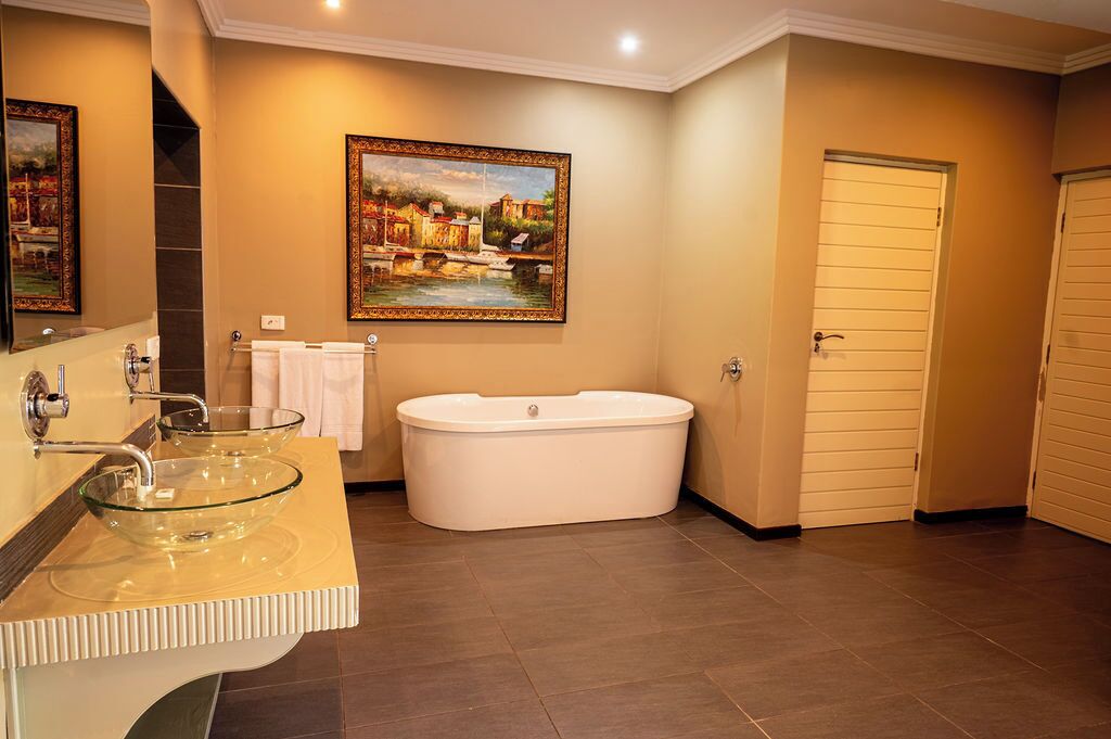 A bathroom with a glass bowl sink, a freestanding bathtub, and a painting of a riverside scene.