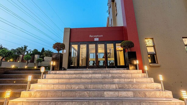 L’entrée d’un hôtel, avec une façade rouge, des portes en verre et des marches menant à l’intérieur.