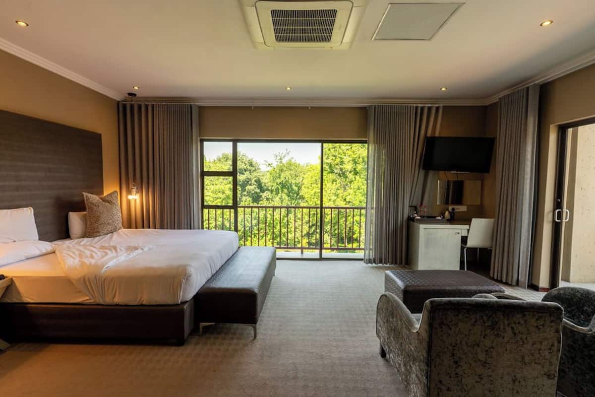 Hotelkamer met een groot bed, een bureau, een televisie en een balkon met uitzicht op bomen.