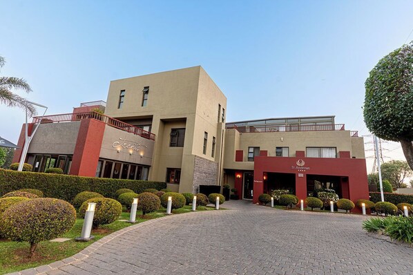 A modern hotel with a central entrance, a red and beige facade, and well-maintained landscaping. - St Andrews Boutique Hotel (Germiston)