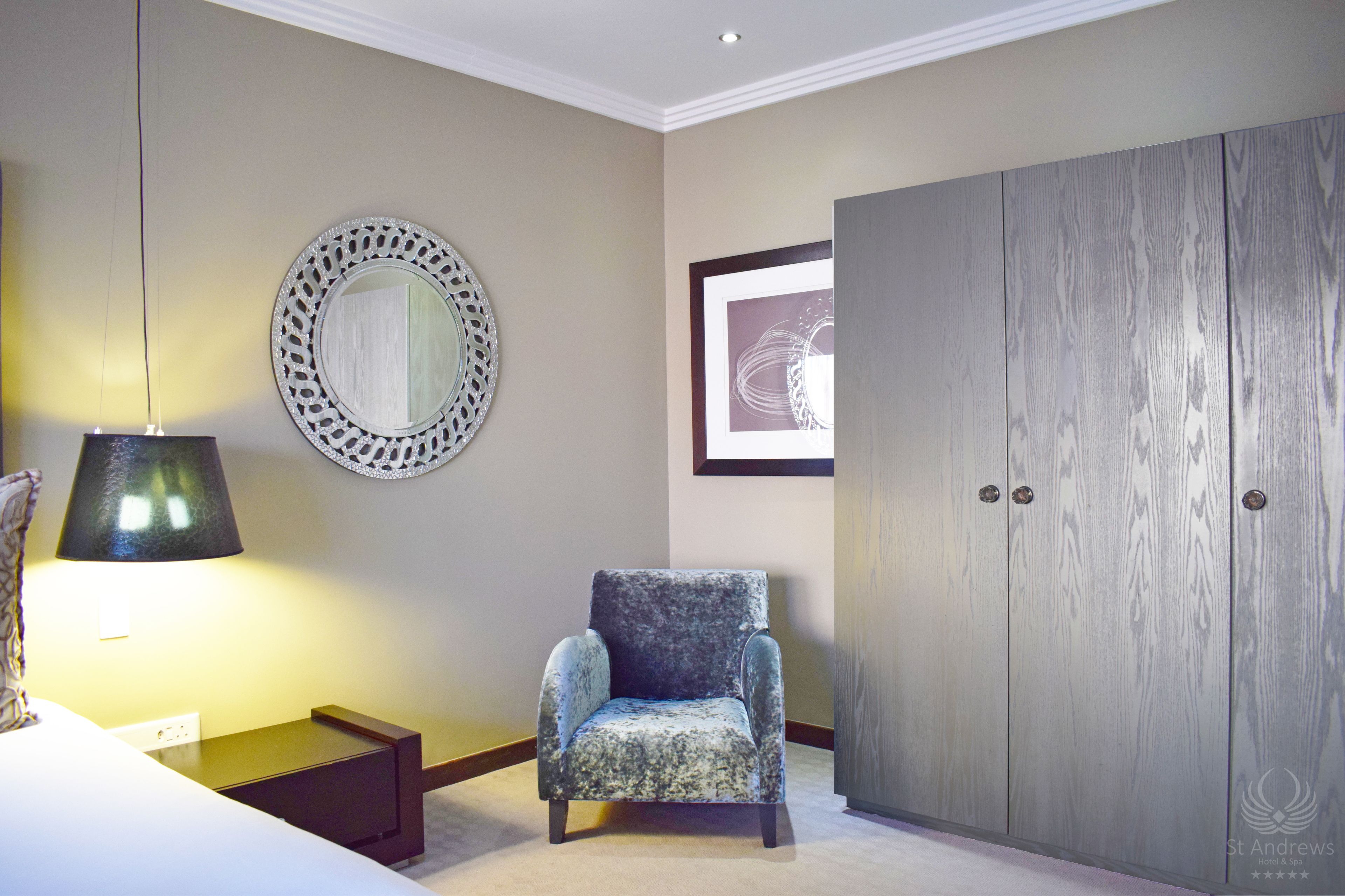 A room with a bed, a chair, a lamp, a mirror, and a wardrobe.