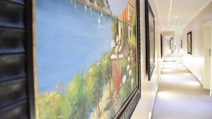 Un couloir orné d’un grand tableau représentant un paysage, doté d’un sol carrelé et de tableaux encadrés accrochés aux murs.