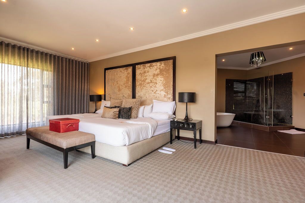 Un dormitorio moderno con una cama grande, mesitas de noche, un cofre rojo para guardar objetos y una zona de ducha con cerramiento de cristal.